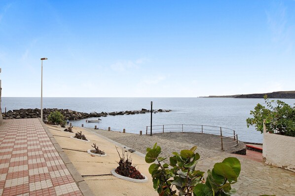 Un paseo marítimo con un camino empedrado, un rompeolas rocoso y una vista despejada del mar.
