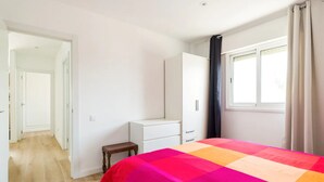 Un dormitorio con cama, armario, banco y ventana con cortinas.