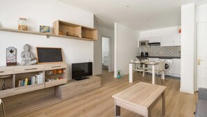 Una sala moderna con un televisor de pantalla plana, estanterías de madera, una pequeña estatua de Buda y un comedor con mesa y sillas.