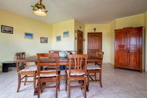 A dining room with a wooden table and chairs, a cabinet, and a cross on the wall. - Holiday Home "Villa Pitti" with Sea View, Terraces & Wi-Fi (Castelsardo)
