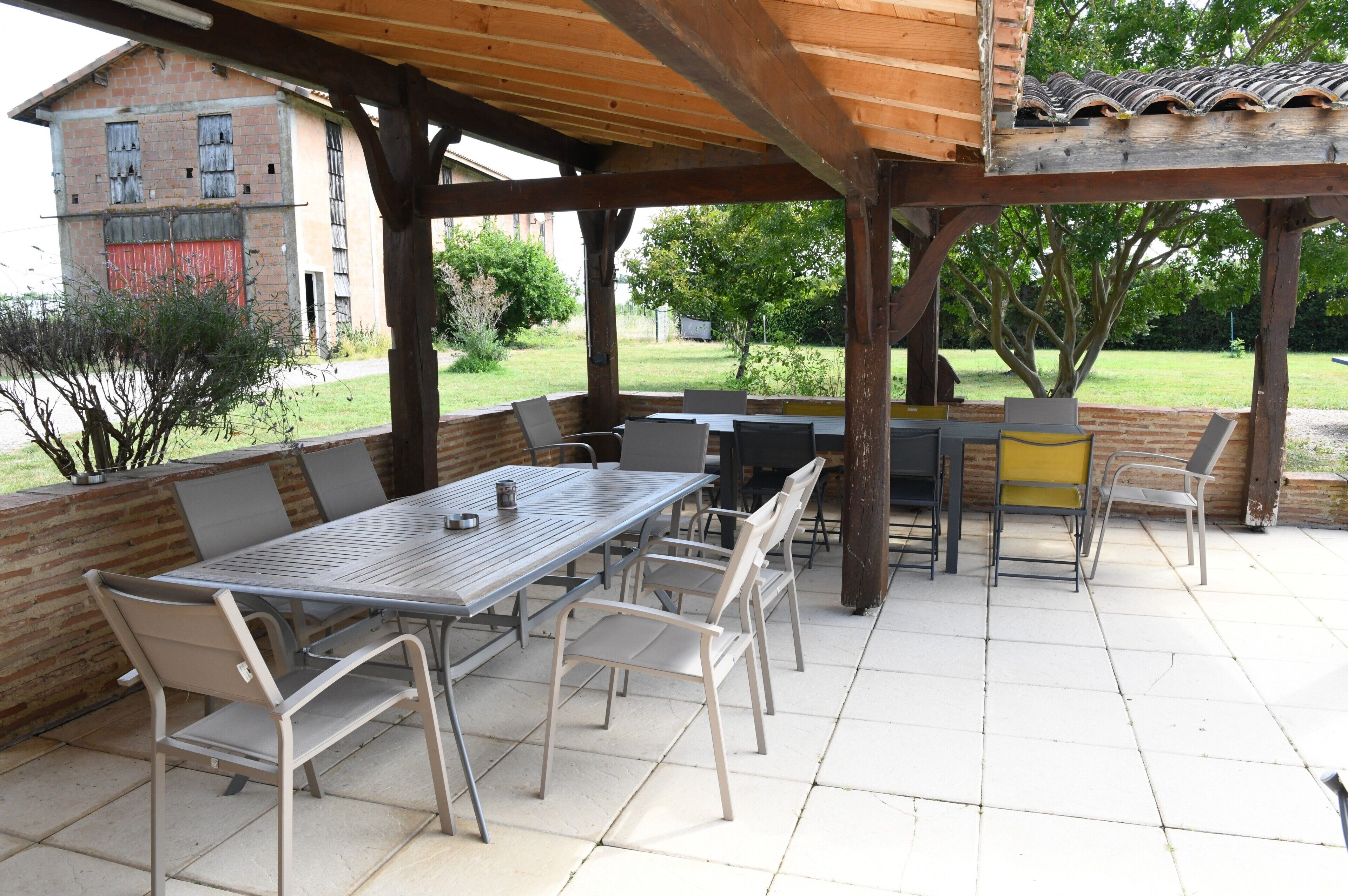 Een terras buiten met een houten pergola, een tafel met stoelen en een bakstenen muur.