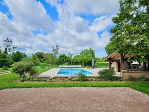 A rectangular swimming pool with a wooden deck, surrounded by a grassy area and trees.