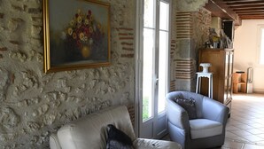 Een kamer met een stenen muur, een witte leren bank, een grijze fauteuil en een schilderij van bloemen.