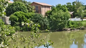 Een gebouw met een rood dak, omgeven door weelderige begroeiing en een rustig waterlichaam.
