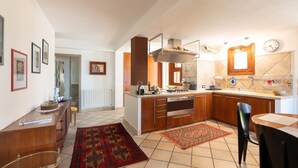 A modern kitchen with wooden cabinets, a built-in stove, and a dining area with a chair. - Villa "Water Front Scopello" with Sea View, Private Beach Access, Garden, and Wi-Fi (Scopello)