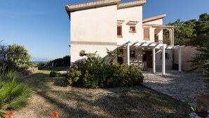 A two-story building with a covered patio, stone pathway, and surrounding greenery. - Villa "Water Front Scopello" with Sea View, Private Beach Access, Garden, and Wi-Fi (Scopello)