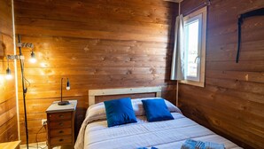 Une pièce aux murs lambrissés, comprenant un lit, une table de chevet, une lampe et une fenêtre.