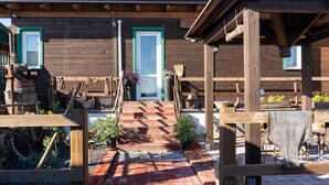 Un bâtiment en bois avec une porte verte, un escalier menant à l’entrée et des espaces extérieurs aménagés pour s’asseoir.