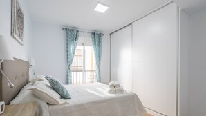 Une chambre à coucher avec un lit, une table de chevet, une lampe, des rideaux et une vue sur l’extérieur.