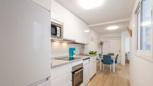 Une cuisine moderne avec des meubles blancs, un four à micro-ondes encastré et un lave-vaisselle. On y trouve également un coin repas avec une table et des chaises bleues.