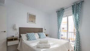 Un lit bien fait, avec des oreillers, une table de chevet avec une lampe, une horloge murale et une fenêtre avec des rideaux.