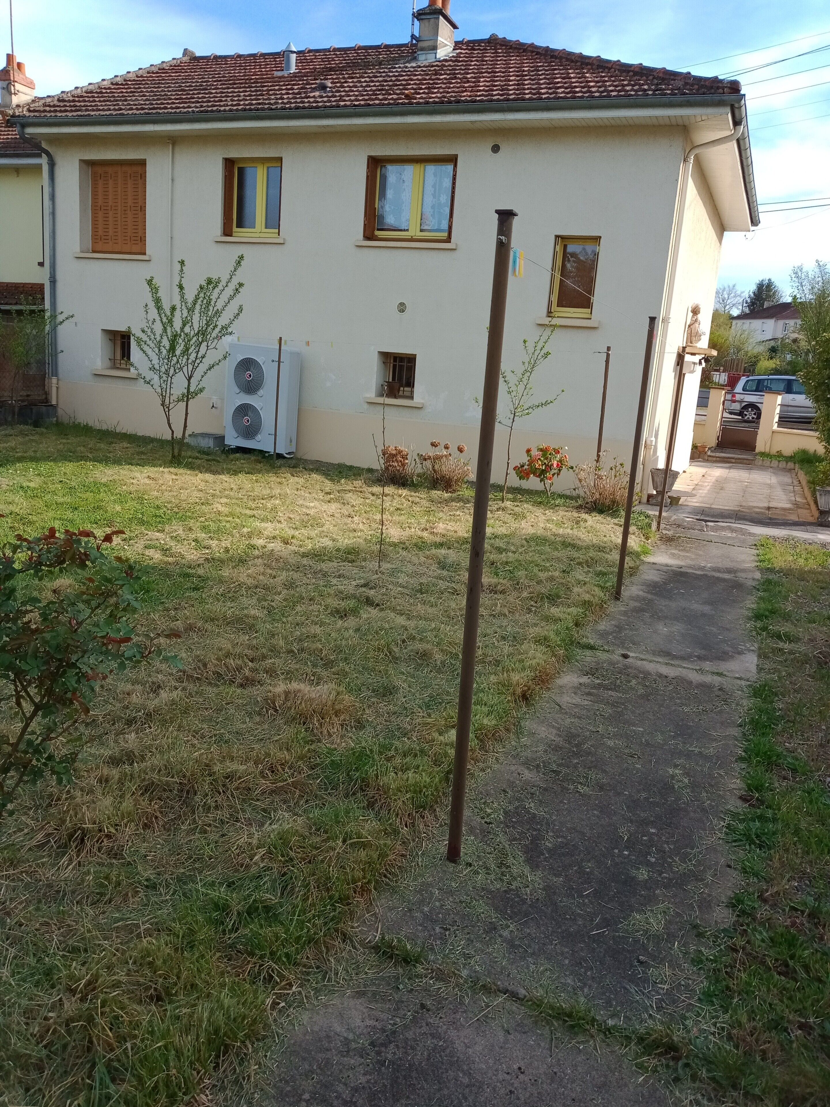 Una casa de dos pisos con techo de tejas, un pequeño jardín y un camino que lleva a la entrada.