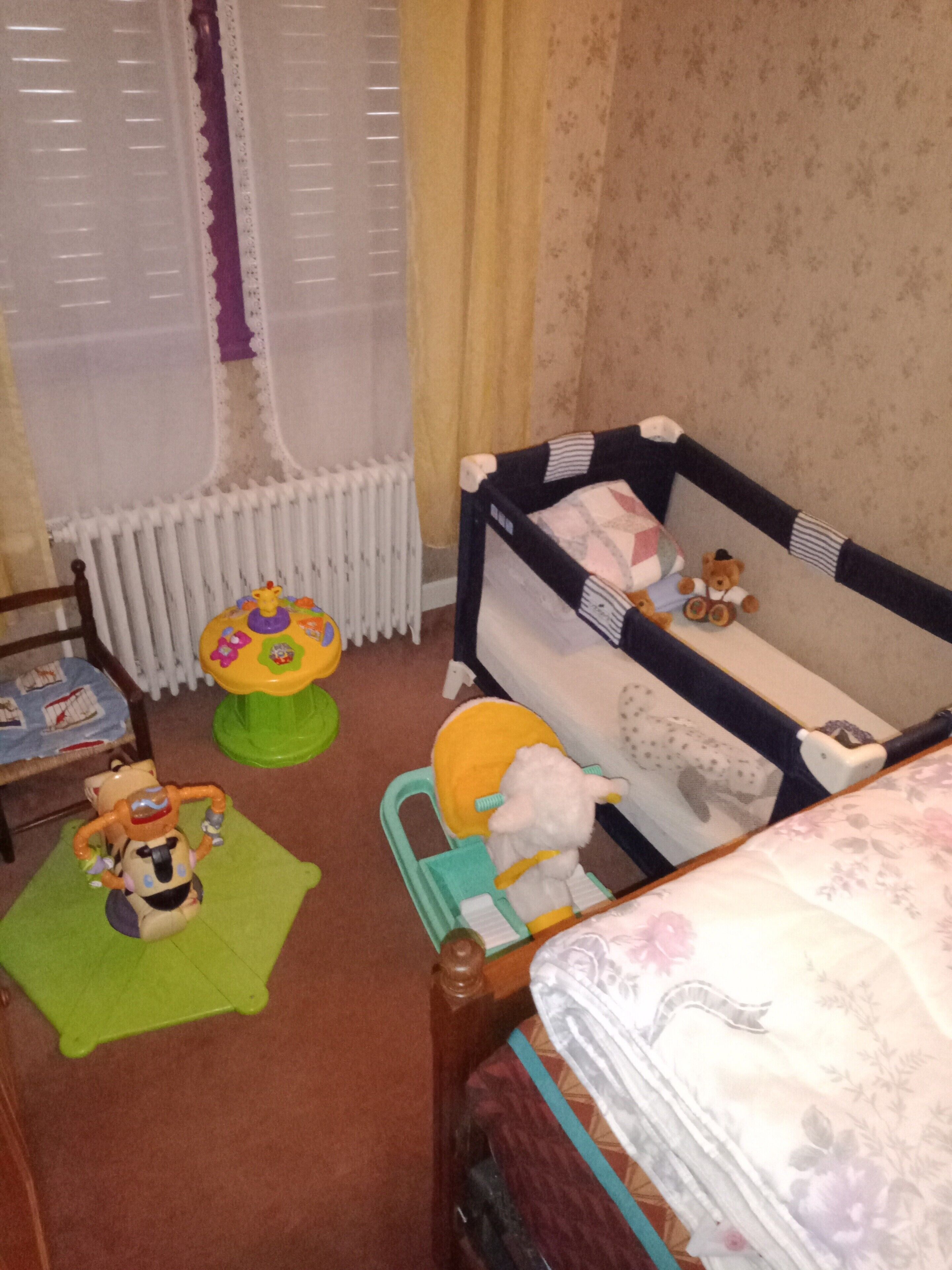 Quarto de bebê com berço, trocador, baú de brinquedos e uma cadeira de madeira.