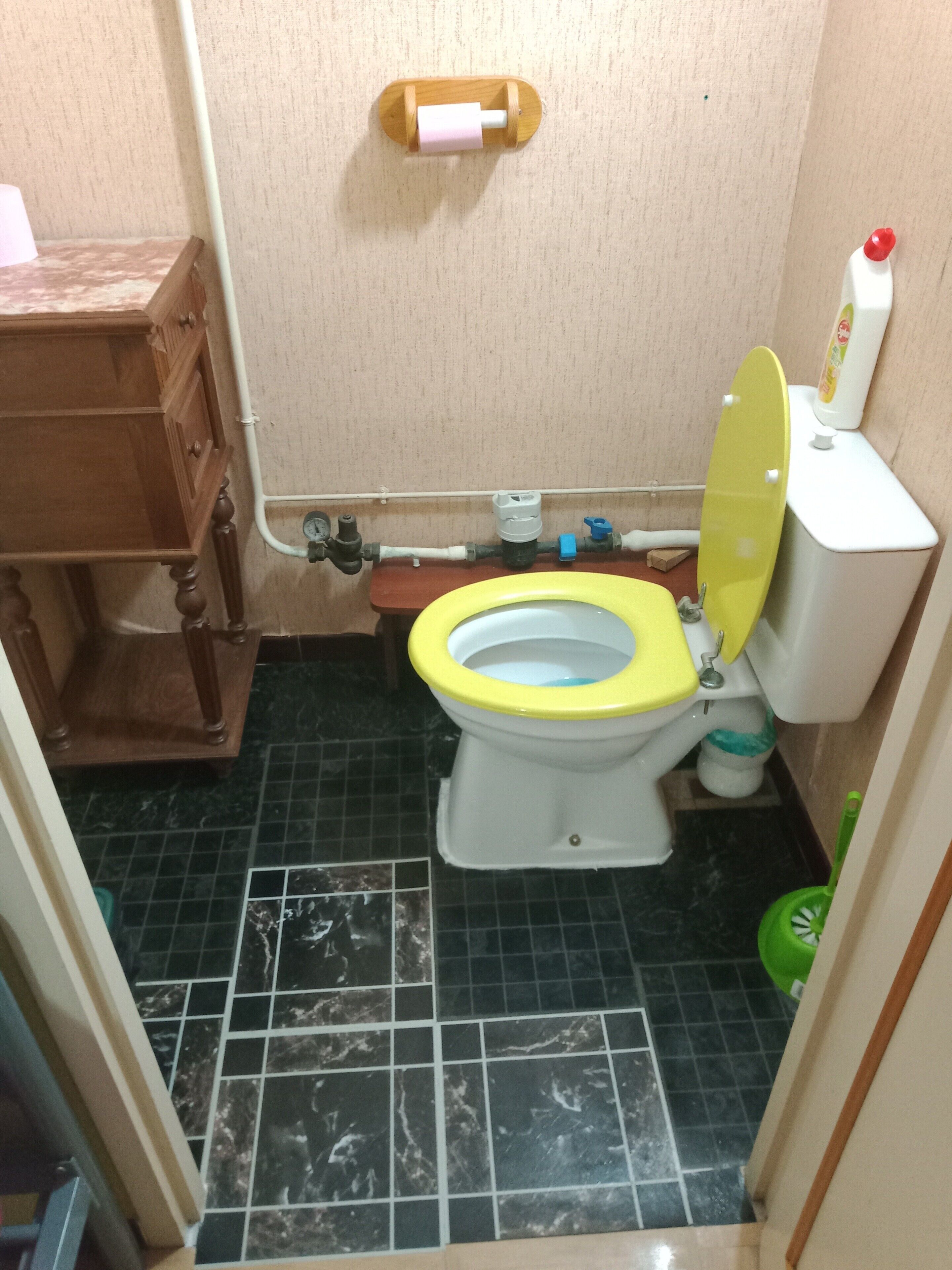 Ein Badezimmer mit Toilette, einem Holzkabinent, einem marmorboden und einem an der Wand befestigten Toilettenpapierhalter.