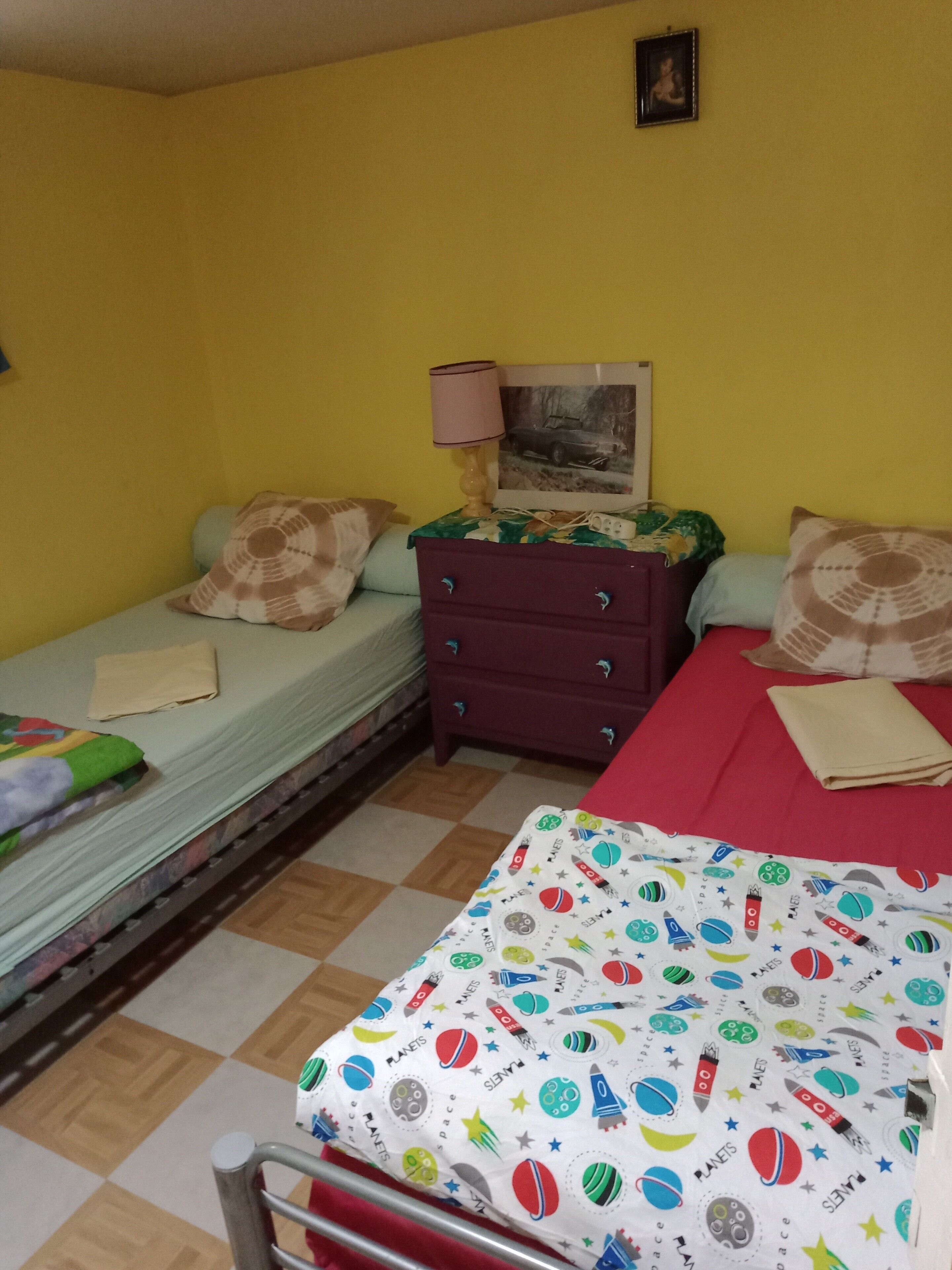 Ein Zimmer mit einem Bett, einem Schminktisch, einem Nachttisch, einer Lampe und einem gerahmten Bild an der Wand.