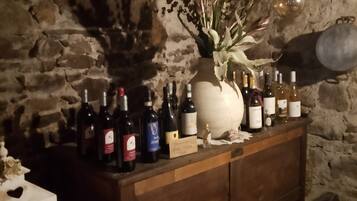 Un intérieur avec un mur en pierre et un bar en bois où sont exposées des bouteilles de vin, ainsi qu’un vase contenant des fleurs séchées.