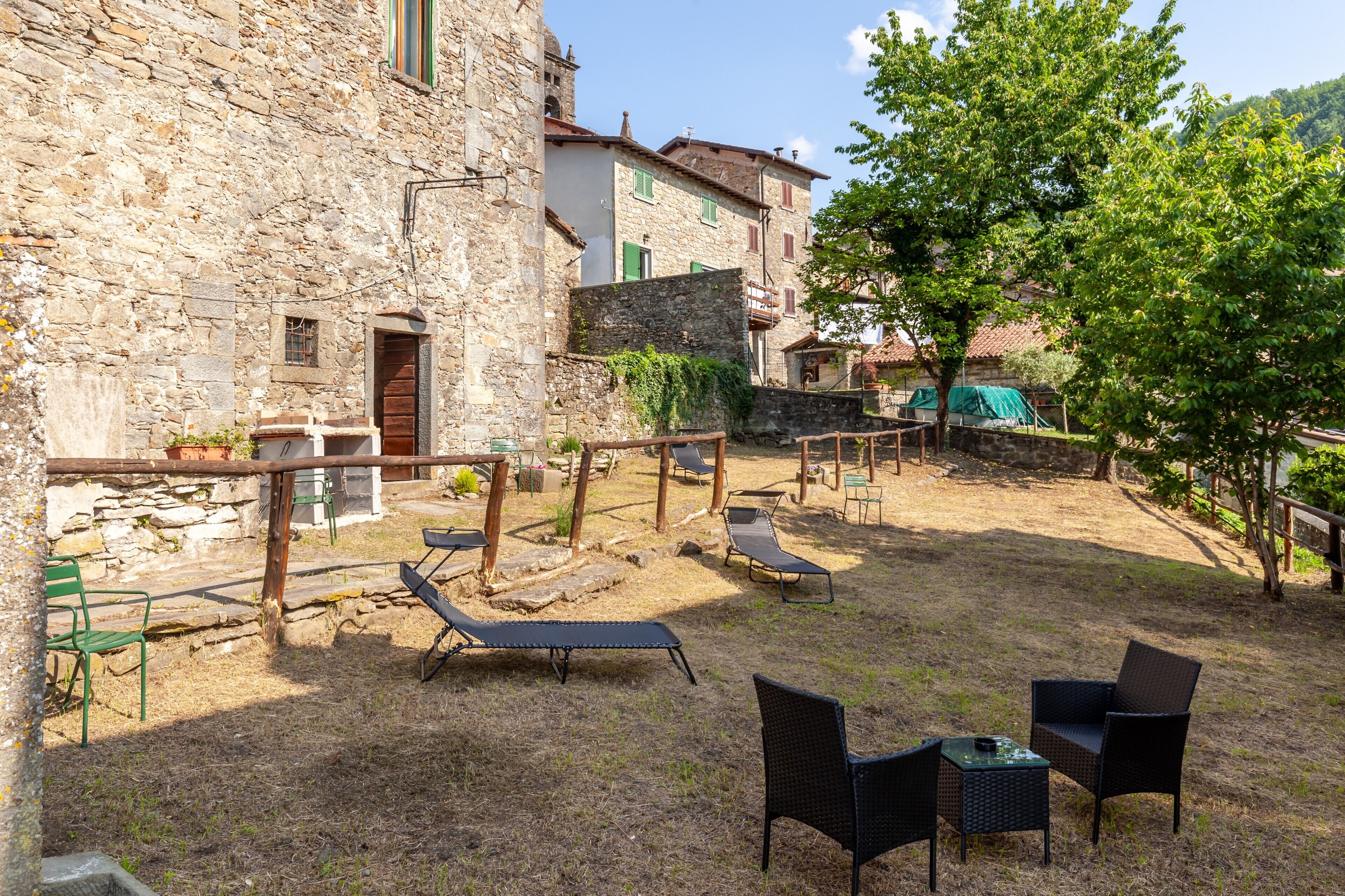 Une cour avec des murs en pierre, du mobilier d’extérieur et un arbre.
