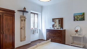 Quarto com cama, guarda-roupa de madeira, penteadeira e uma pequena mesa com espelho.