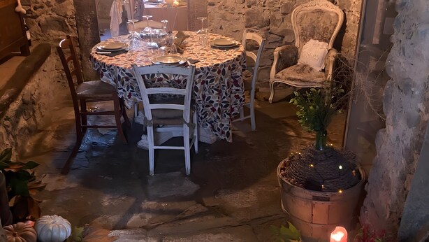 Quarto com paredes de pedra, mesa de jantar posta para dois, planta em vaso e uma cadeira.