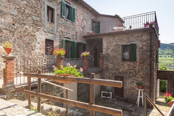 A stone building with a balcony, potted plants, and a view of the countryside.