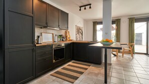 A modern kitchen with dark cabinetry, a central island, and a dining area with a view. - Holiday Home "El Cine" with Mountain View, Pool & Wi-Fi (Canillas de Albaida)