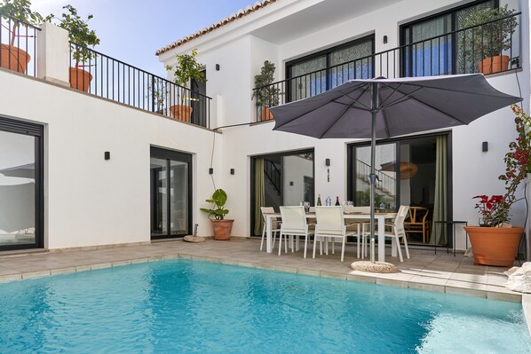 Un espace aménagé au bord de la piscine, comprenant une table à manger, des chaises et un grand parasol.