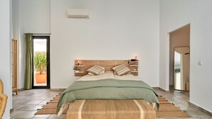 A bedroom with a wooden headboard, a green blanket, a woven bench, and a view of the outdoors through a door. - Holiday Home "El Cine" with Mountain View, Pool & Wi-Fi (Canillas de Albaida)