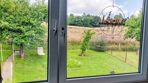 Une vue à travers une fenêtre sur un jardin avec une pelouse, des arbres et un portail en métal.
