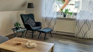 Un salon moderne avec un fauteuil bleu foncé, une petite table d’appoint avec une lampe et une table basse en bois.