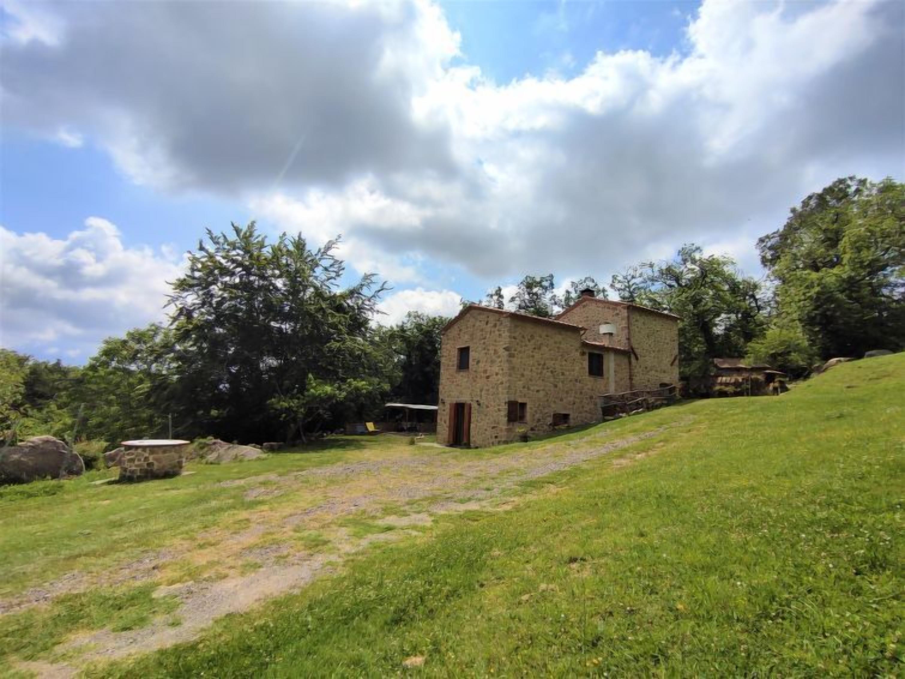 A rustic stone building with a sloped roof, surrounded by a grassy area and trees.