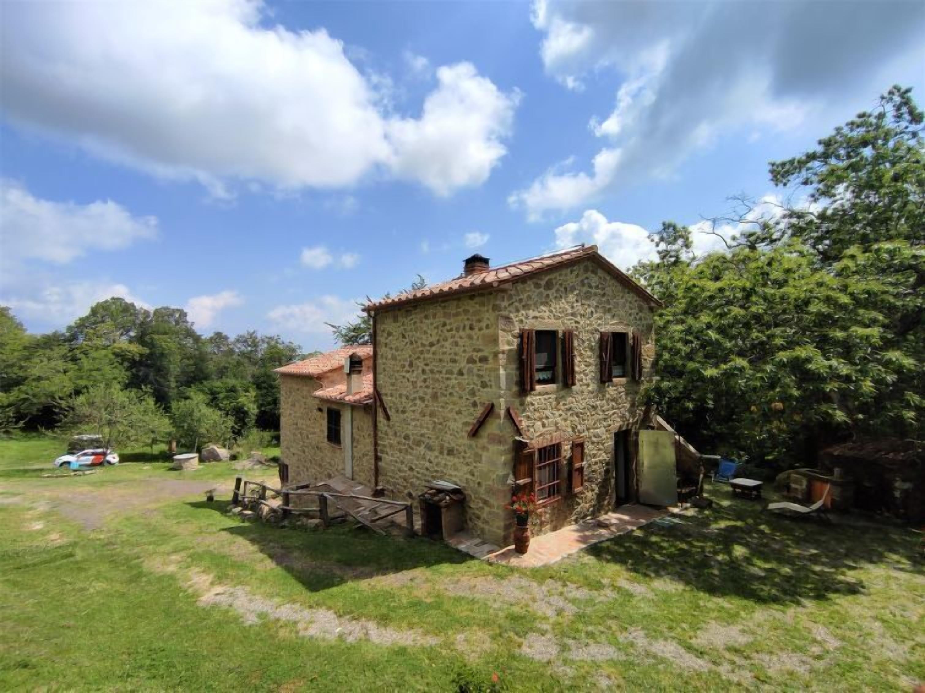Ein Steinhaus mit einem Ziegeldach, umgeben von einem grünen Rasen und Bäumen.