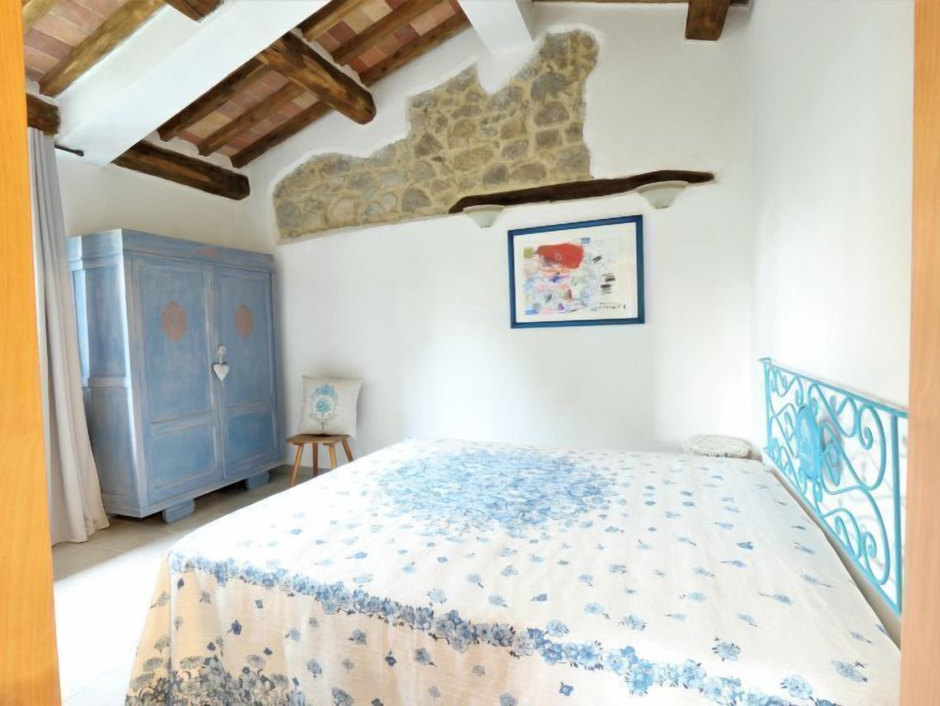 Une chambre à coucher avec un lit, une armoire bleue, un mur en pierre et un tableau encadré accroché au mur.