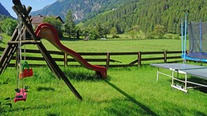 A playground with a slide and swings in a grassy field with a mountain backdrop.