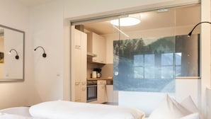 Una camera da letto moderna con un letto grande, una porta in vetro che dà su una cucina e vista su una foresta dalla finestra.