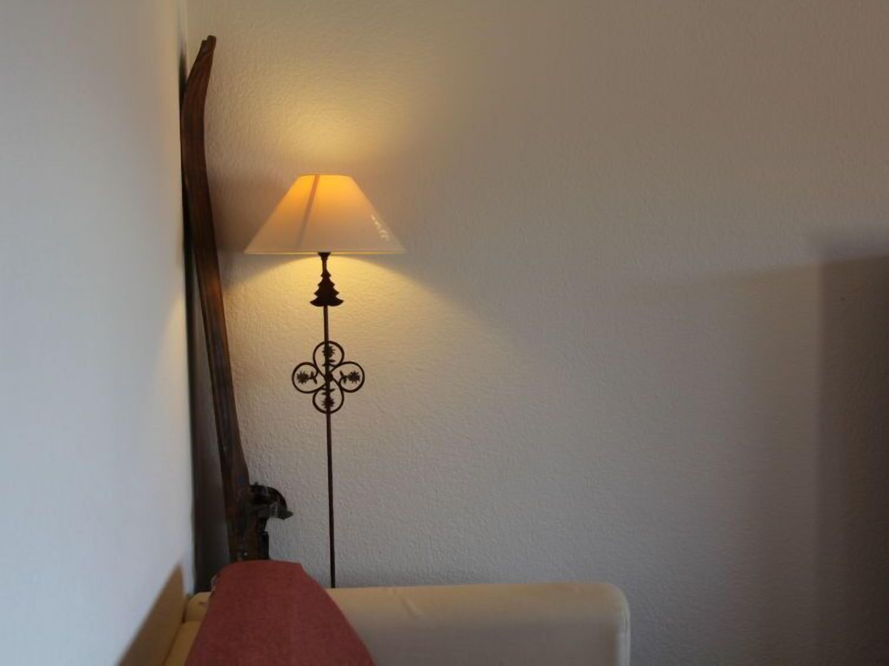 A corner of a room with a white wall, a wooden chair, and a floor lamp with a white lampshade.