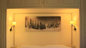 A bedroom with a bed, two wall-mounted lamps, and a painting of a snowy landscape. - Les Girolles B15 by Interhome (Villars)