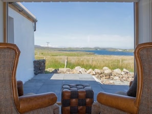 Une pièce avec deux fauteuils en cuir placés face à un mur de pierre, offrant une vue sur un lac et des collines.