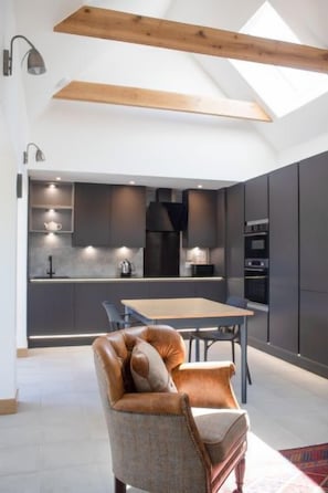 Une cuisine moderne avec des meubles de couleur sombre, un plafond en bois et un coin repas comprenant une table et des chaises.