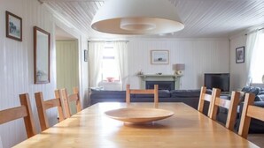 Un coin repas avec une table et des chaises en bois, une cheminée, un téléviseur et un canapé à l’arrière-plan.