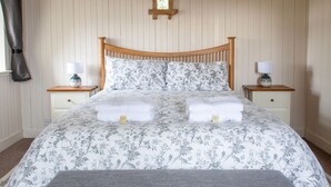 Une chambre à coucher avec un cadre de lit en bois, une literie à motifs floraux, deux tables de chevet avec des lampes et une petite croix en bois accrochée au mur.