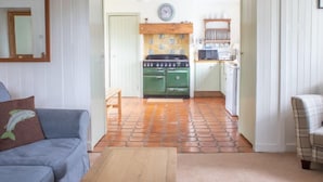 Un salon chaleureux avec un canapé, une table basse et une vue sur une cuisine dotée d’un poêle vert et d’un dosseret carrelé.