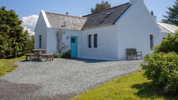 Une petite maison blanche avec une porte turquoise, une allée en gravier et une table de pique-nique.