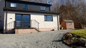 Een woonhuis met twee verdiepingen, een voortuin, een kleine schuur en een grindpad.