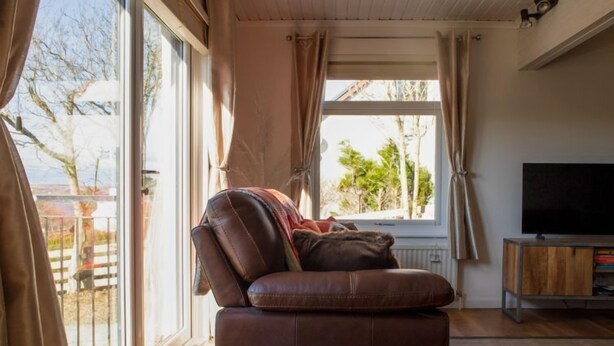 Een gezellige woonkamer met een leren bank, een kleine tafel, een televisie en een raam met gordijnen.