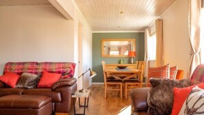 Een gezellige woonkamer met een bruine leren bank, een gestreepte zithoek en een eettafel met stoelen.