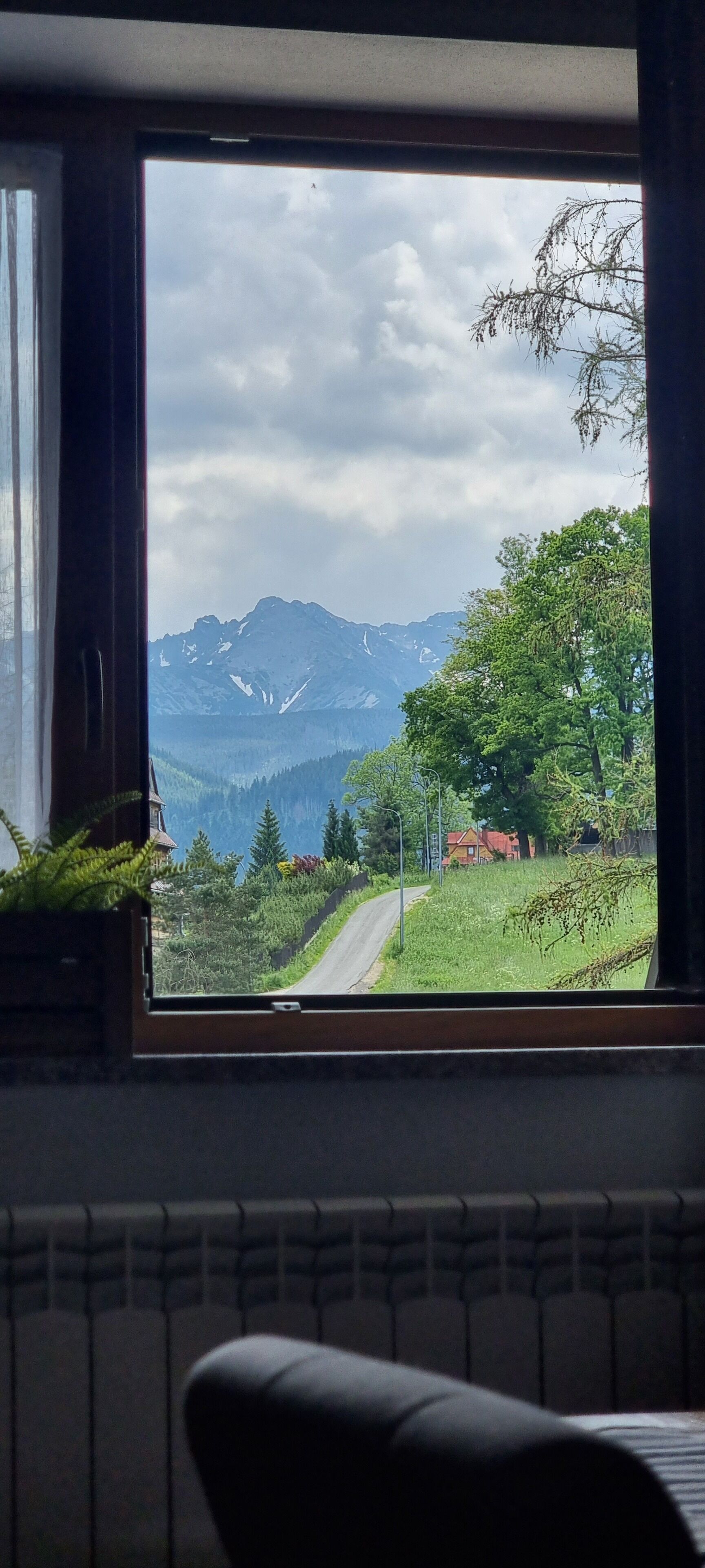 A window view of a mountain landscape with a road, trees, and a house.