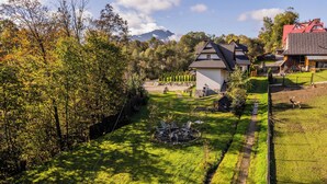Zona residencial amb una casa que té teulada inclinada i una estructura petita adossada. Hi ha un jardí amb gespa, una xemeneia exterior i mobiliari per seure.