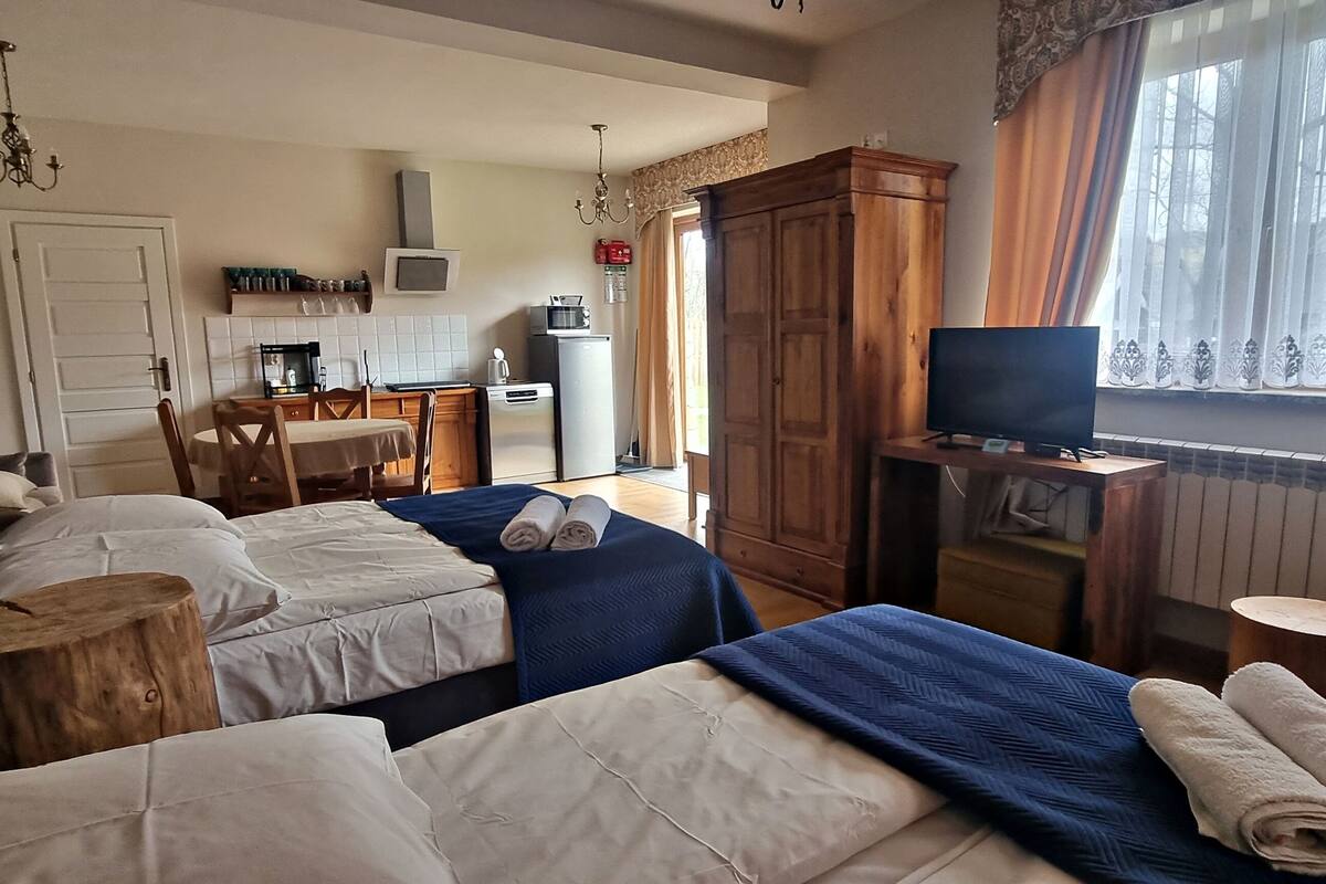 A hotel room with two beds, a dining table, a TV, and a view of the outside.
