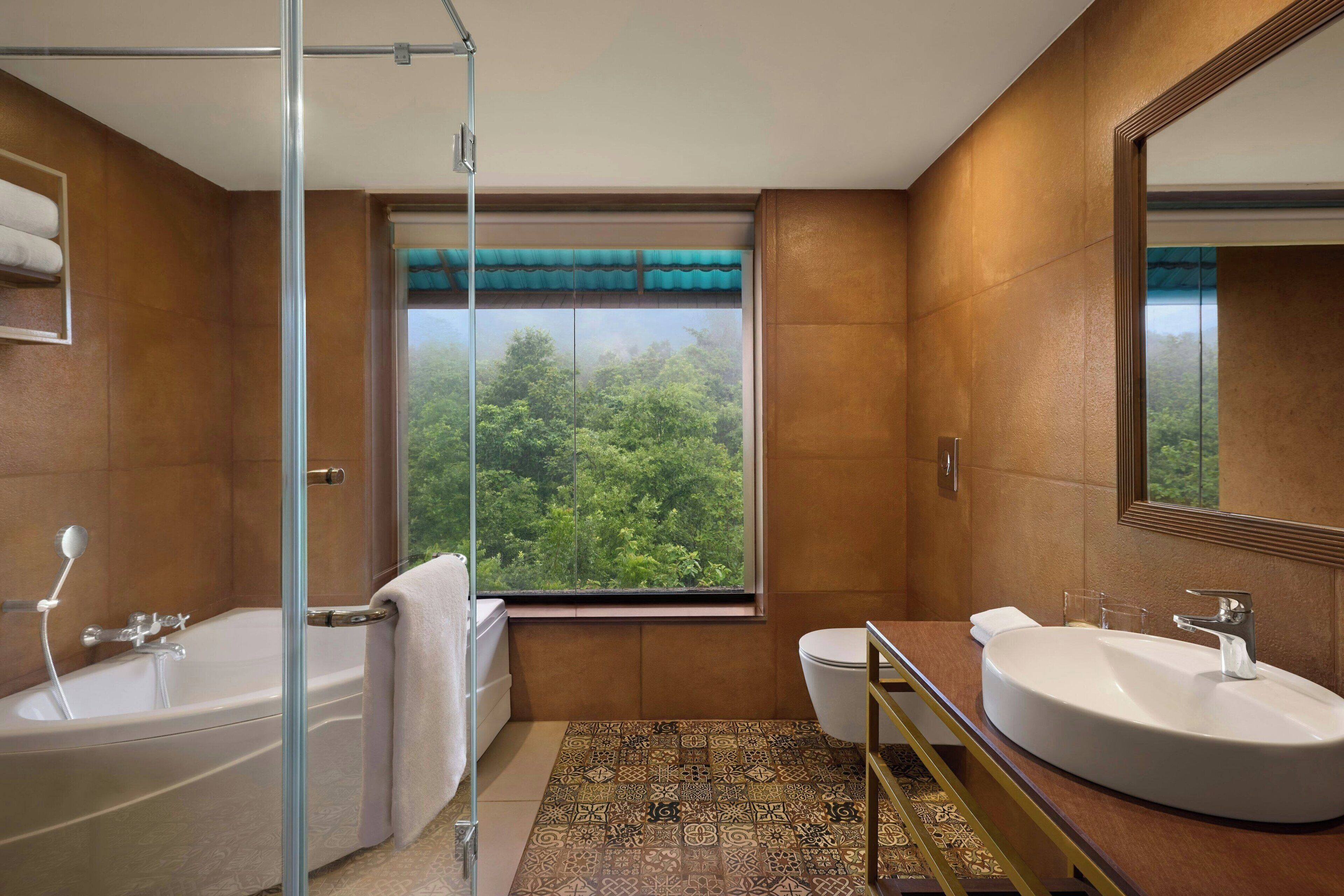 Un baño con bañera, inodoro y lavamanos, que cuenta con un ventanal con vistas a zonas verdes.