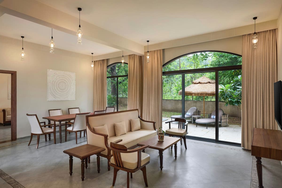 Amplia sala de estar con sofá, mesa de comedor y sillas, ventanas grandes con cortinas y un televisor a la derecha.